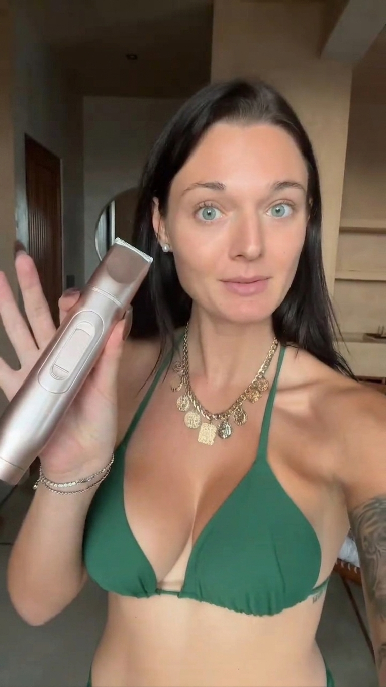 Woman in a green bikini holding a hair trimmer indoors.